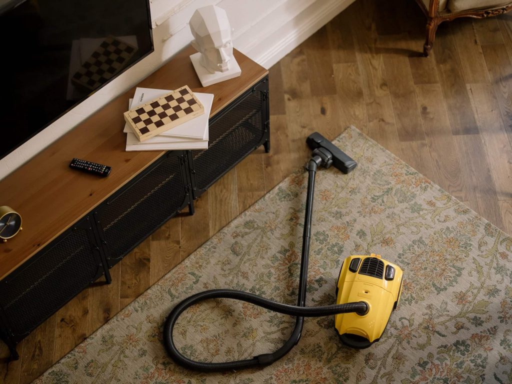 Yellow vacuum cleaner on a oriental rug, over a hardwood floor, and furnishing.